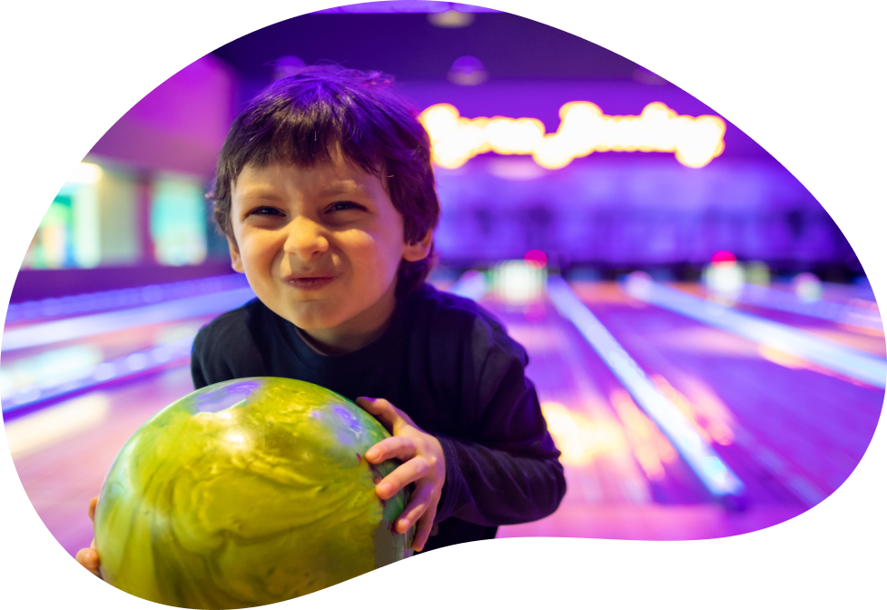 young child holding a bowling ball in a bowling alley